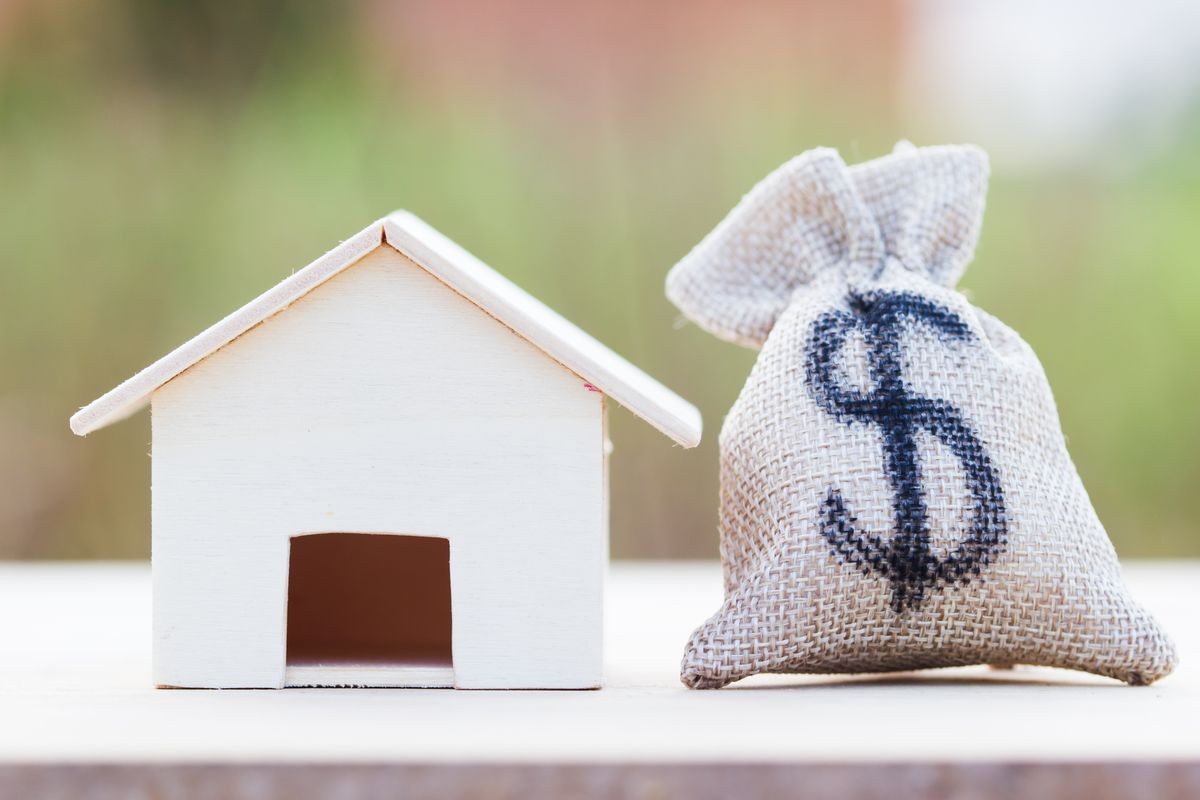 Home loan, mortgages, debt, savings money for home buying concept : US dollar in a money bag, small residential, house model on table against green nature background. Exchange of finances and houses.